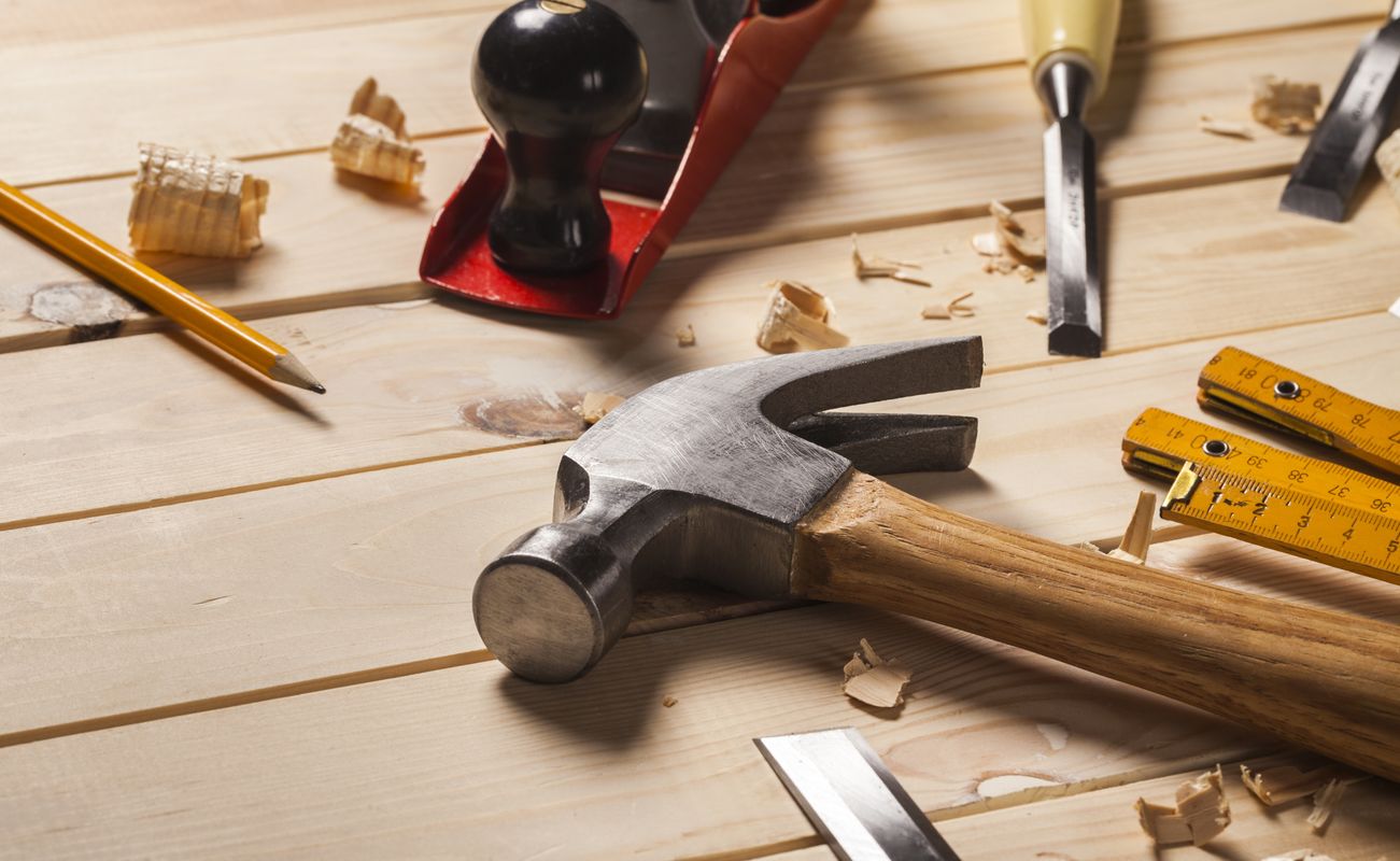 Werkzeuganordnung auf einem Holztisch, einschließlich eines Hammers, eines Hobels, Meißeln, einem Bleistift und Zollstöcken.
